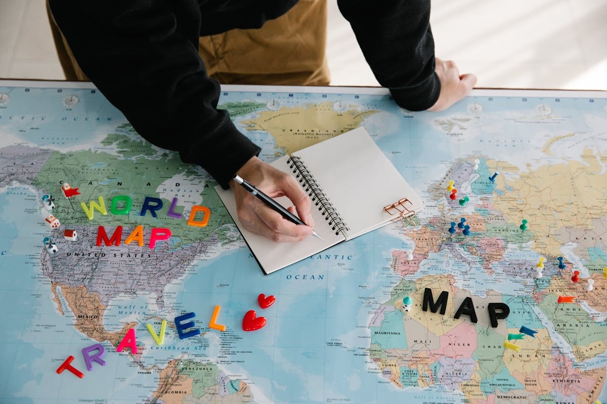 Person writing in notebook on world map planning international travel routes