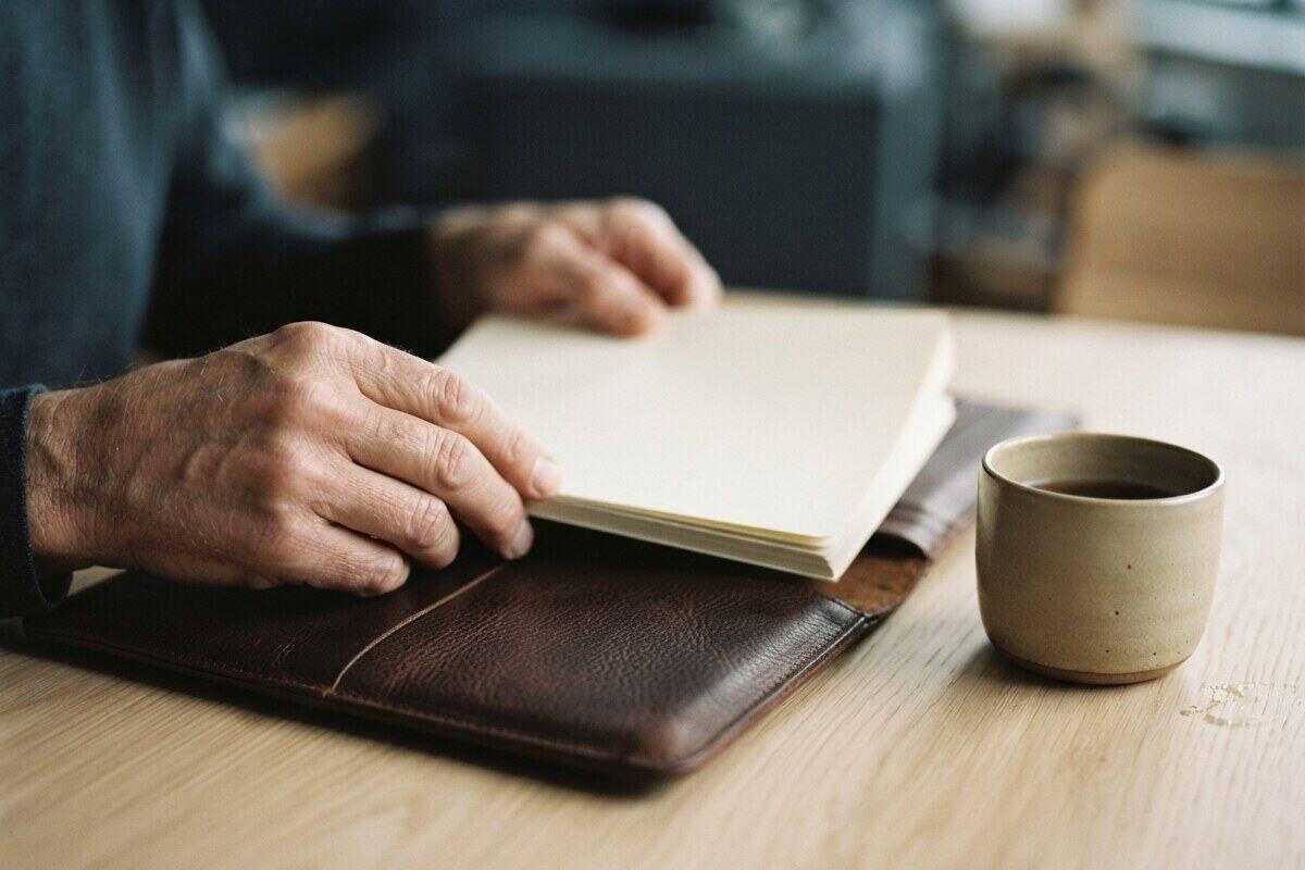 Hands placing blank papers into a leather folio on oak