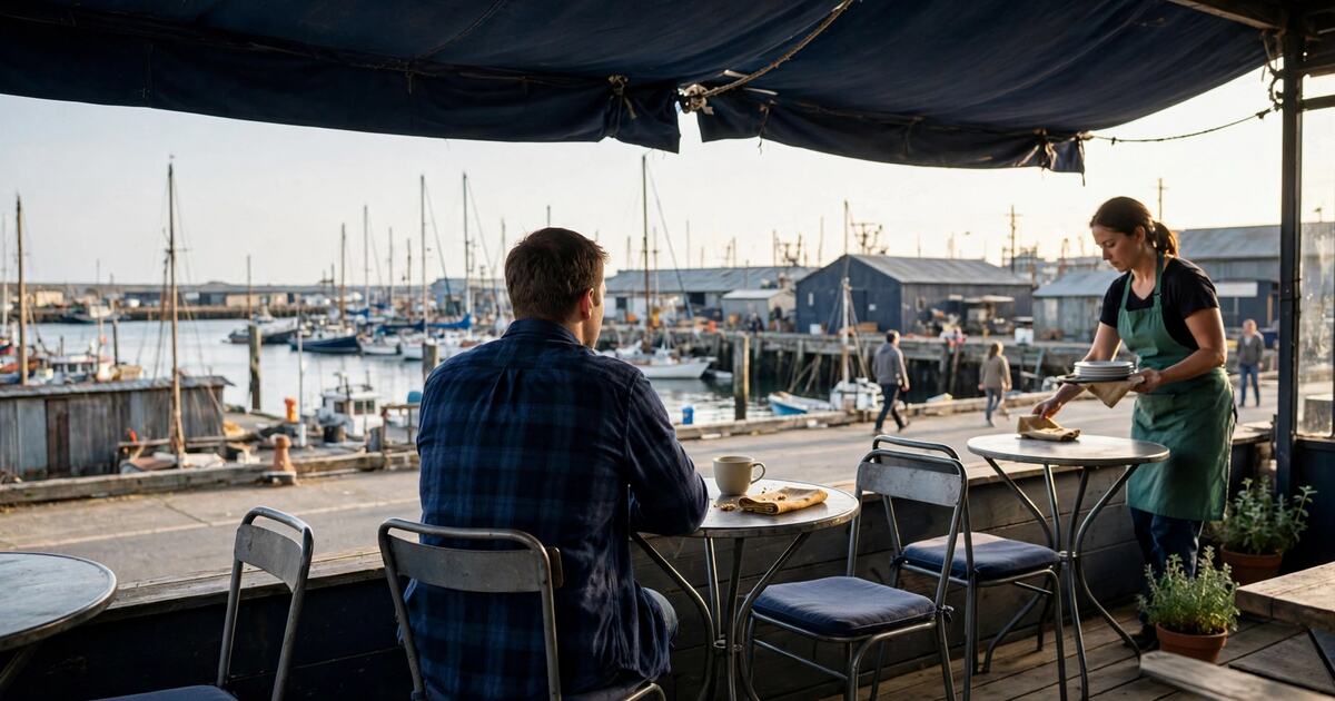 Person seated at a harbor cafe terrace in warm late-afternoon light
